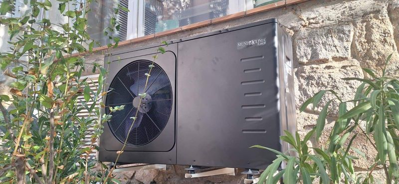 Unidad exterior de aerotermia instalada junto a la fachada de piedra de una vivienda