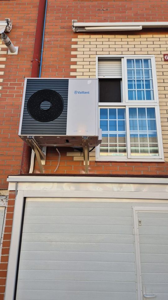 Unidad exterior de aerotermia Vaillant instalada en la fachada de ladrillo de una vivienda, sobre la puerta del garaje
