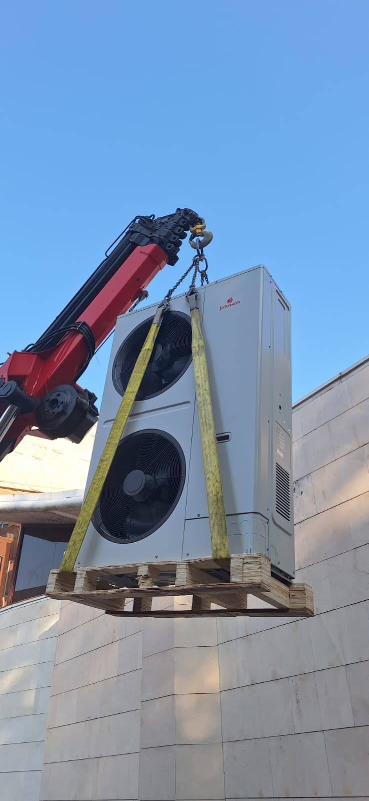 Equipo de Igloo izando con grúa una unidad exterior de climatización hasta la cubierta de un edificio en Madrid